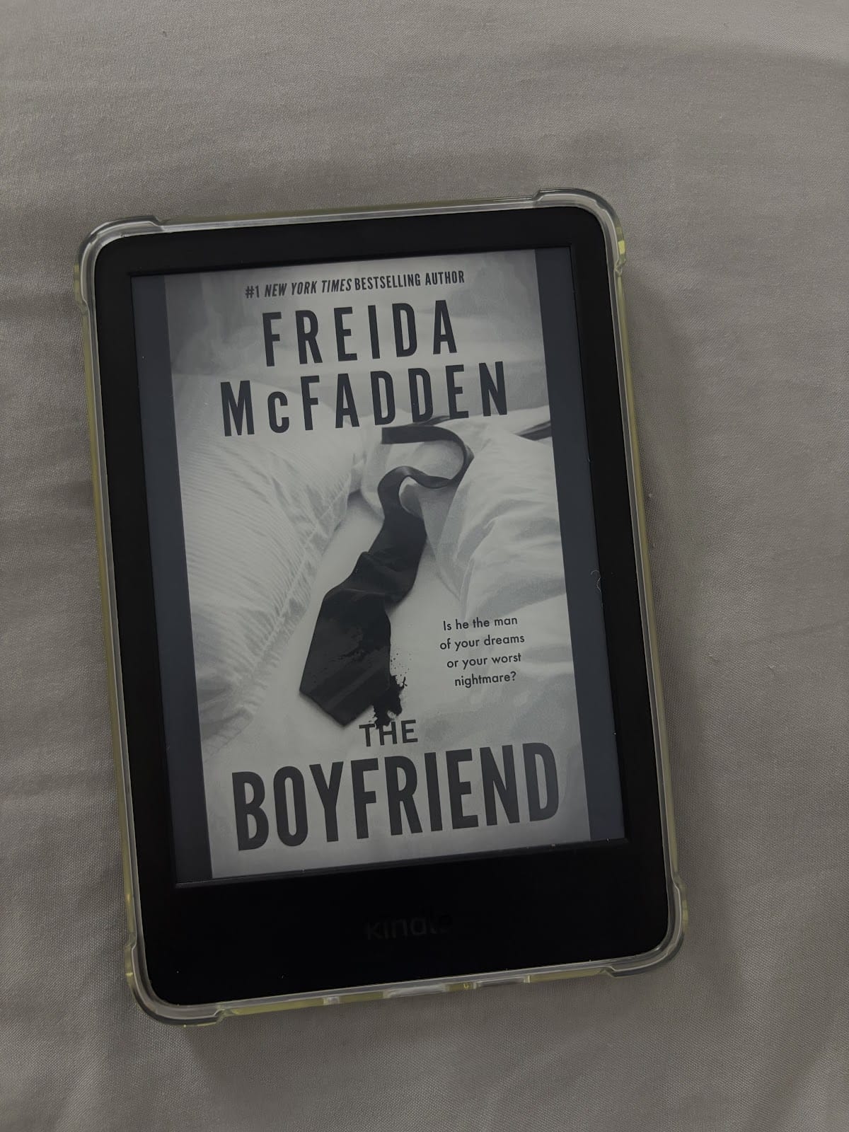 A Kindle e-reader displaying the cover of the book "The Boyfriend" by Freida McFadden. The cover features a black necktie on a white bedspread, with text that reads, "Is he the man of your dreams or your worst nightmare?