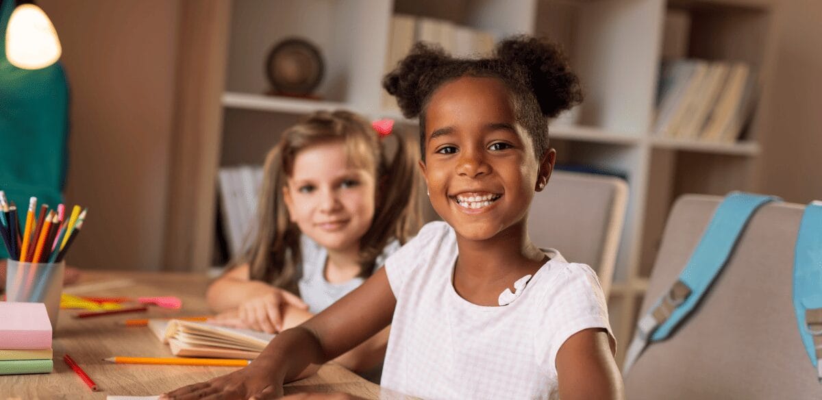 Two children seated at a table, their hands resting on the desk, engaged in a focused activity together.