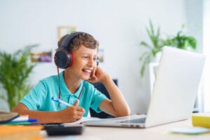 A boy with headphones sits at a desk, focused on his laptop, immersed in his work or entertainment.