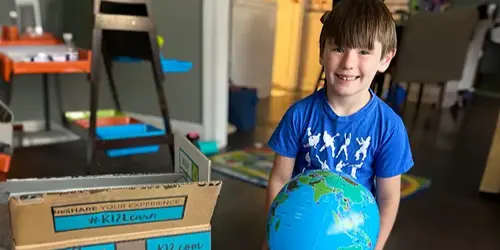 A young boy stands holding a globe, positioned in front of a box, symbolizing curiosity and exploration of the world.