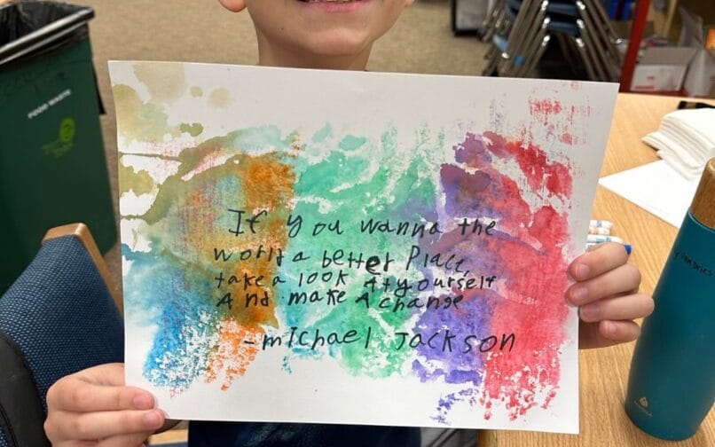 A person proudly holding up their colorful artwork featuring the Michael Jackson quote "If you wanna make the world a better place take a look at yourself and make a change.