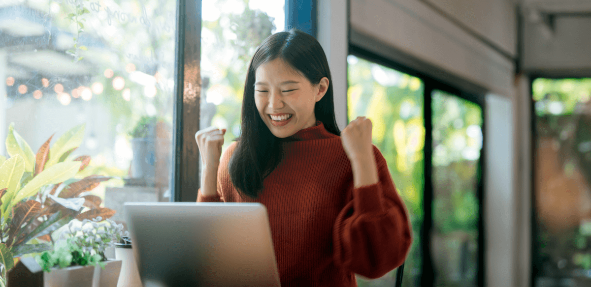 A woman smiles brightly while working on her laptop, showcasing a moment of joy and productivity.